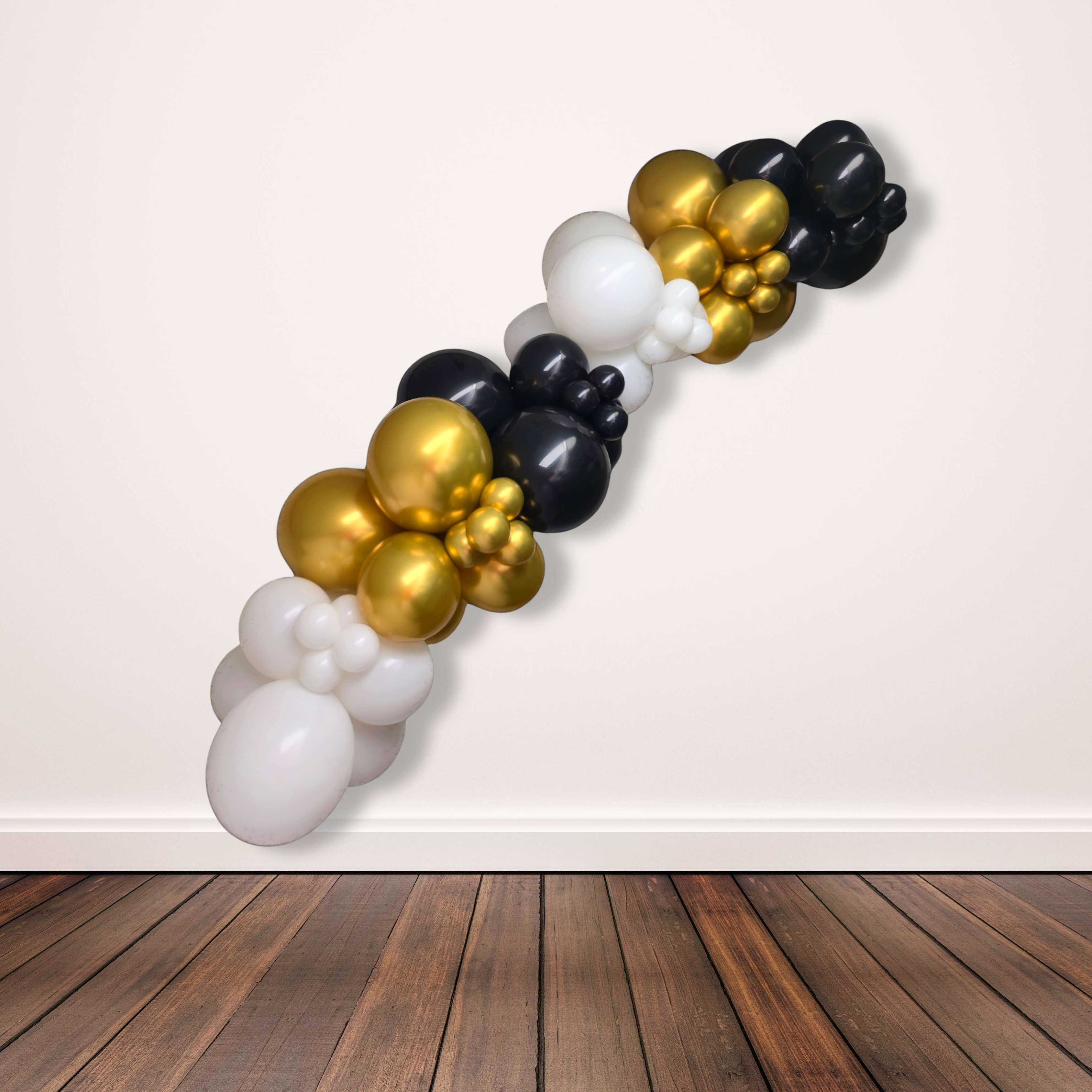 Balloon arch with gold, black, and white balloons against a plain wall.