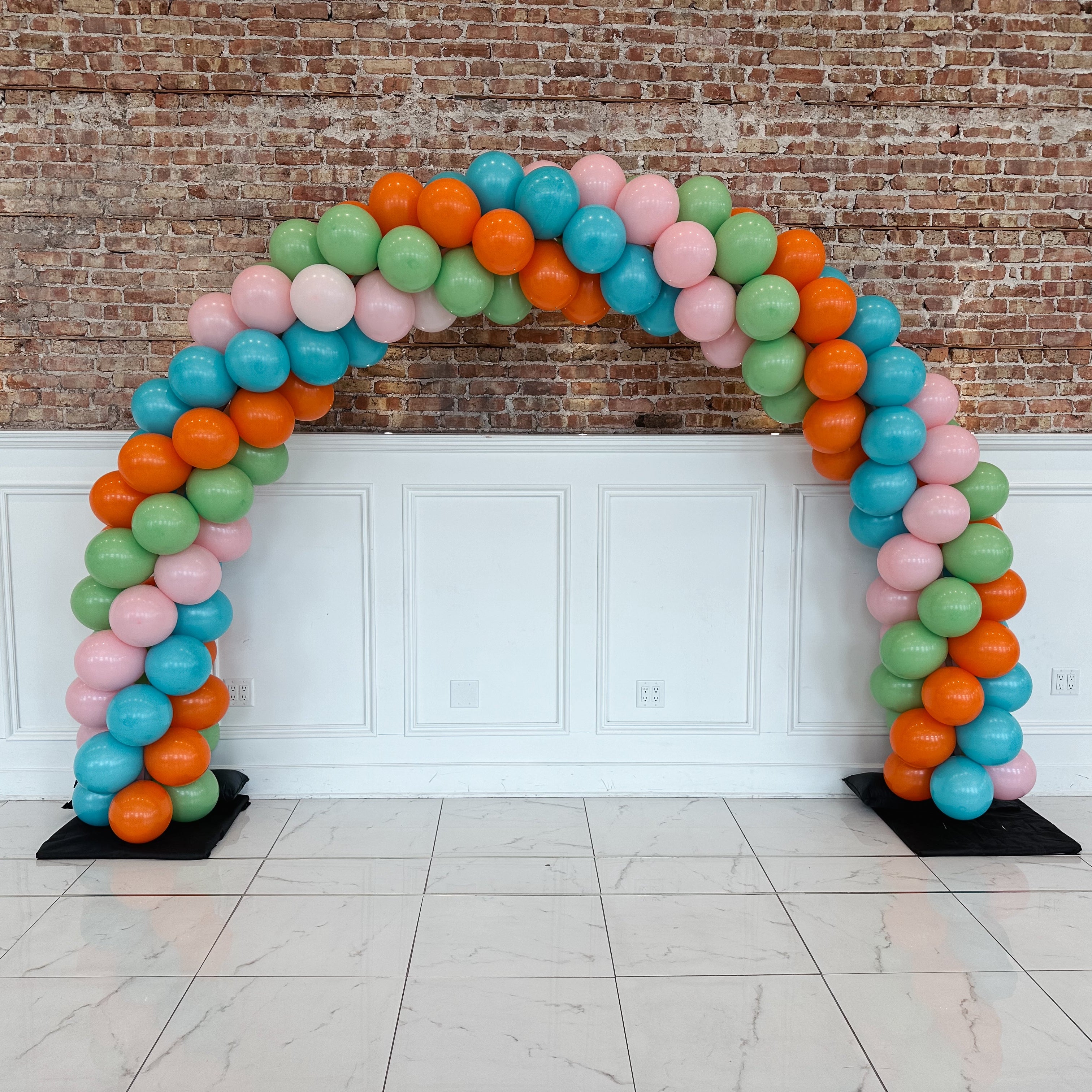 Colorful balloon arch against a brick wall and white paneled wall.