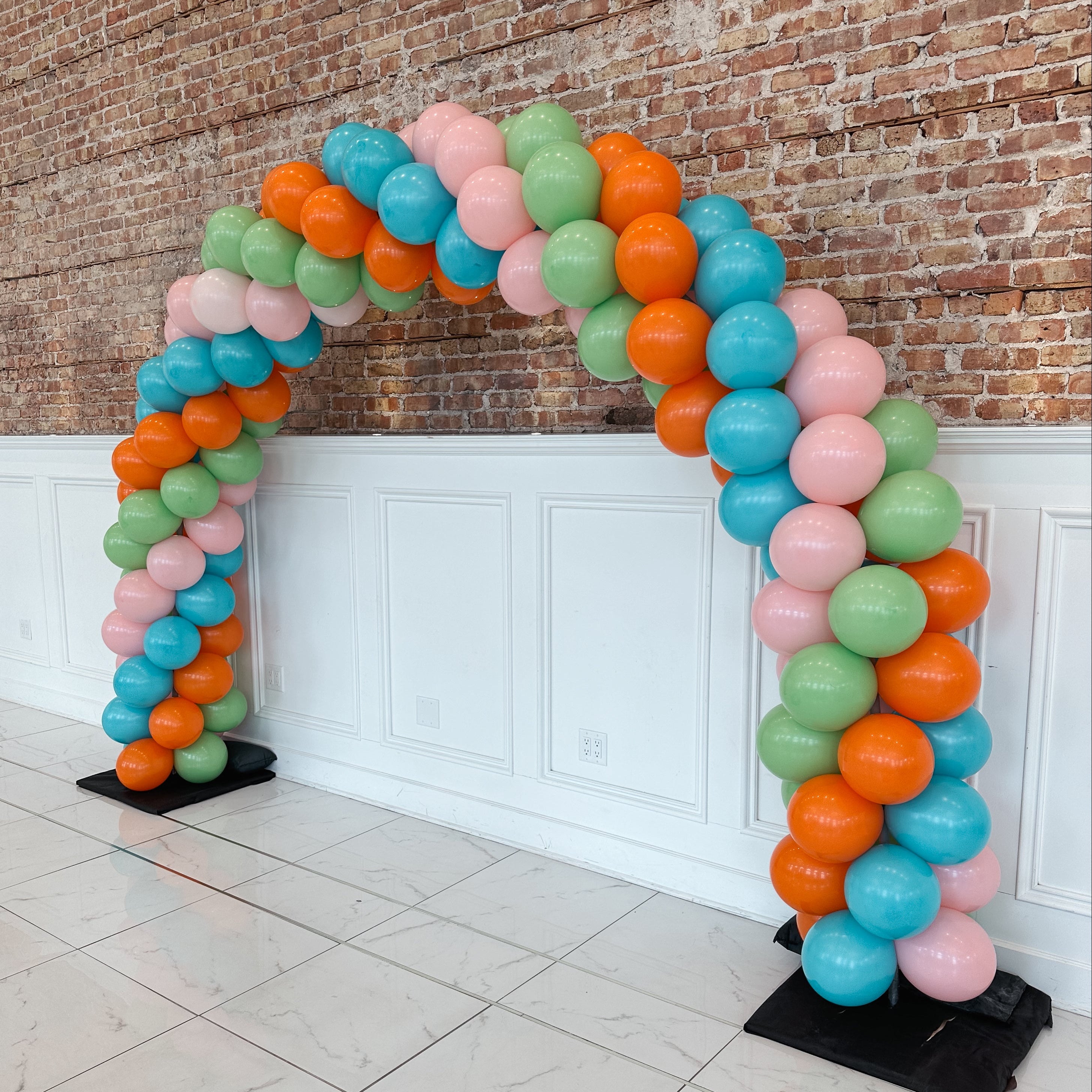 Colorful balloon arch against a brick wall.