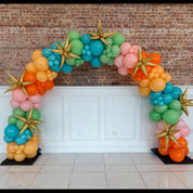 Colorful balloon arch with gold stars against a brick wall.