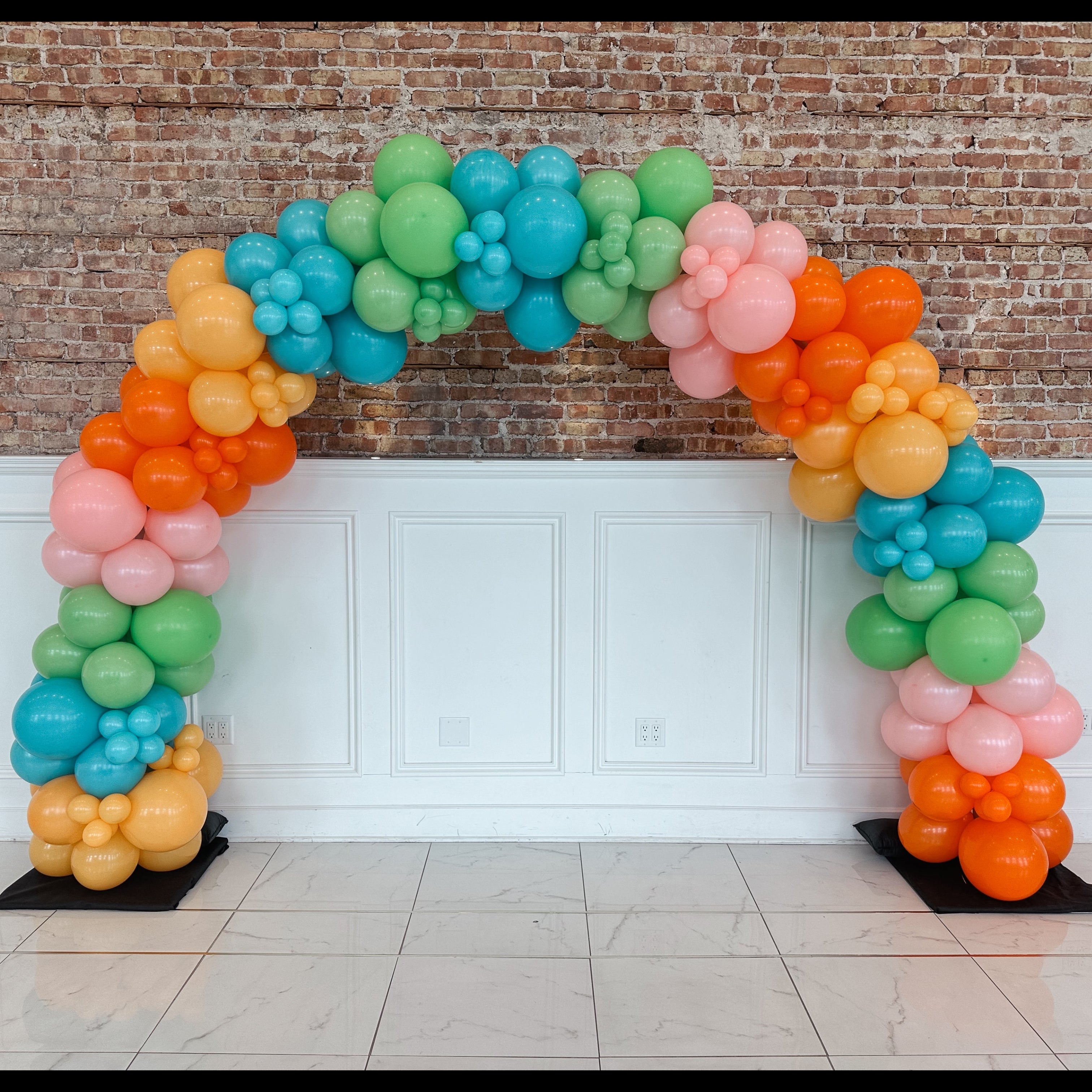 Colorful balloon arch against a brick wall and white paneling.