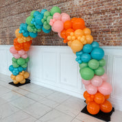 Colorful balloon arch against a brick wall.