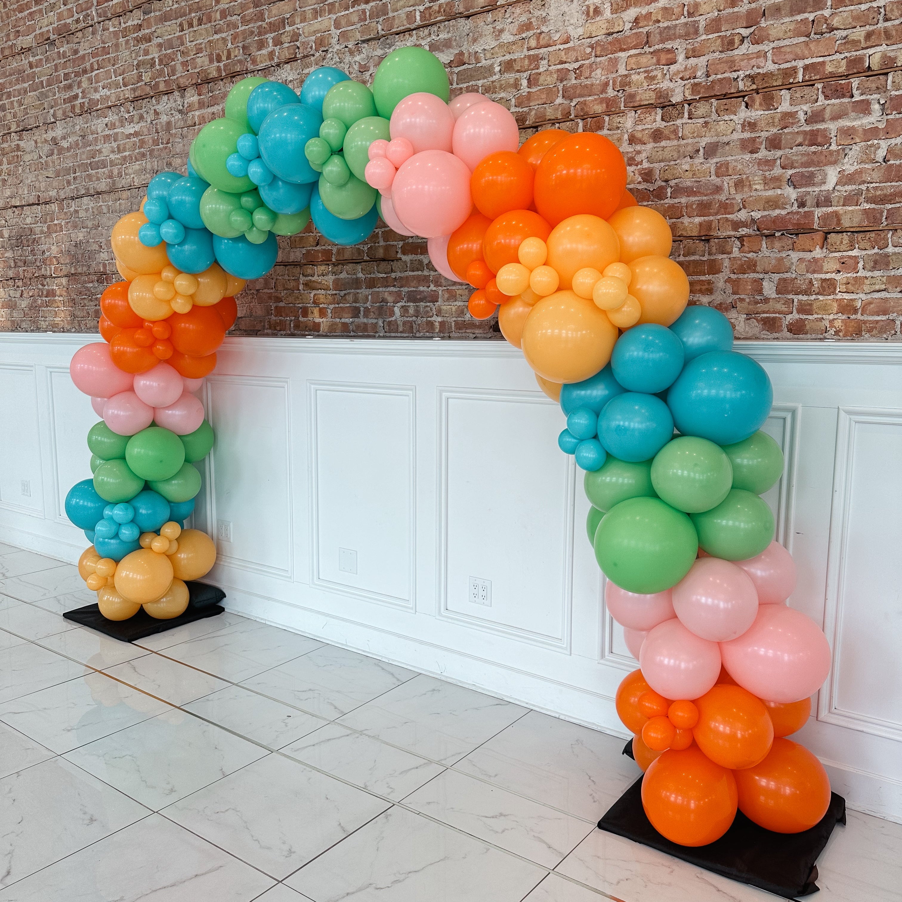 Colorful balloon arch against a brick wall.
