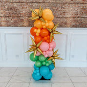 Colorful balloon sculpture with gold stars against a brick wall.