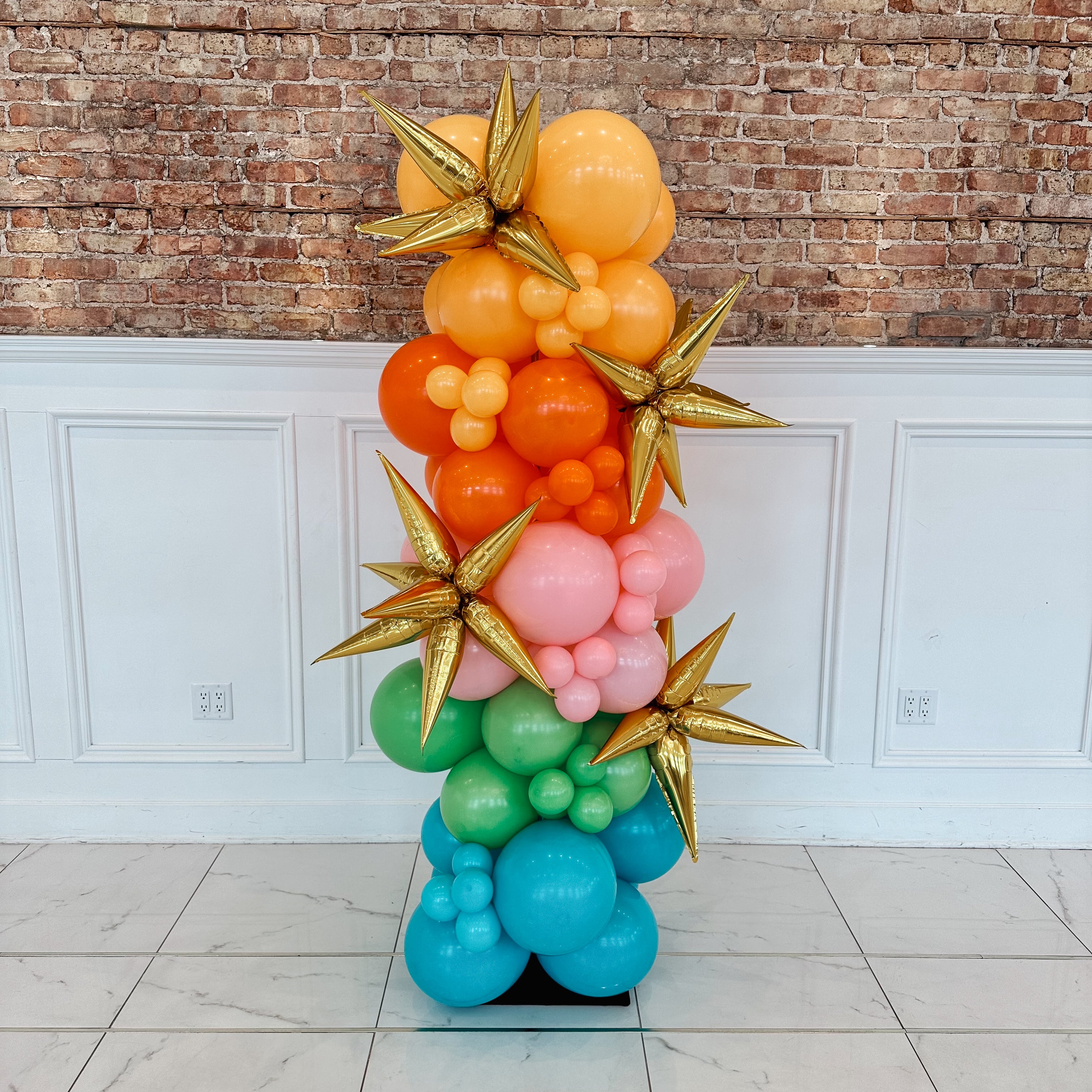 Colorful balloon sculpture with gold stars against a brick wall.