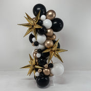 Balloon arch with black, gold, and white balloons on a plain background