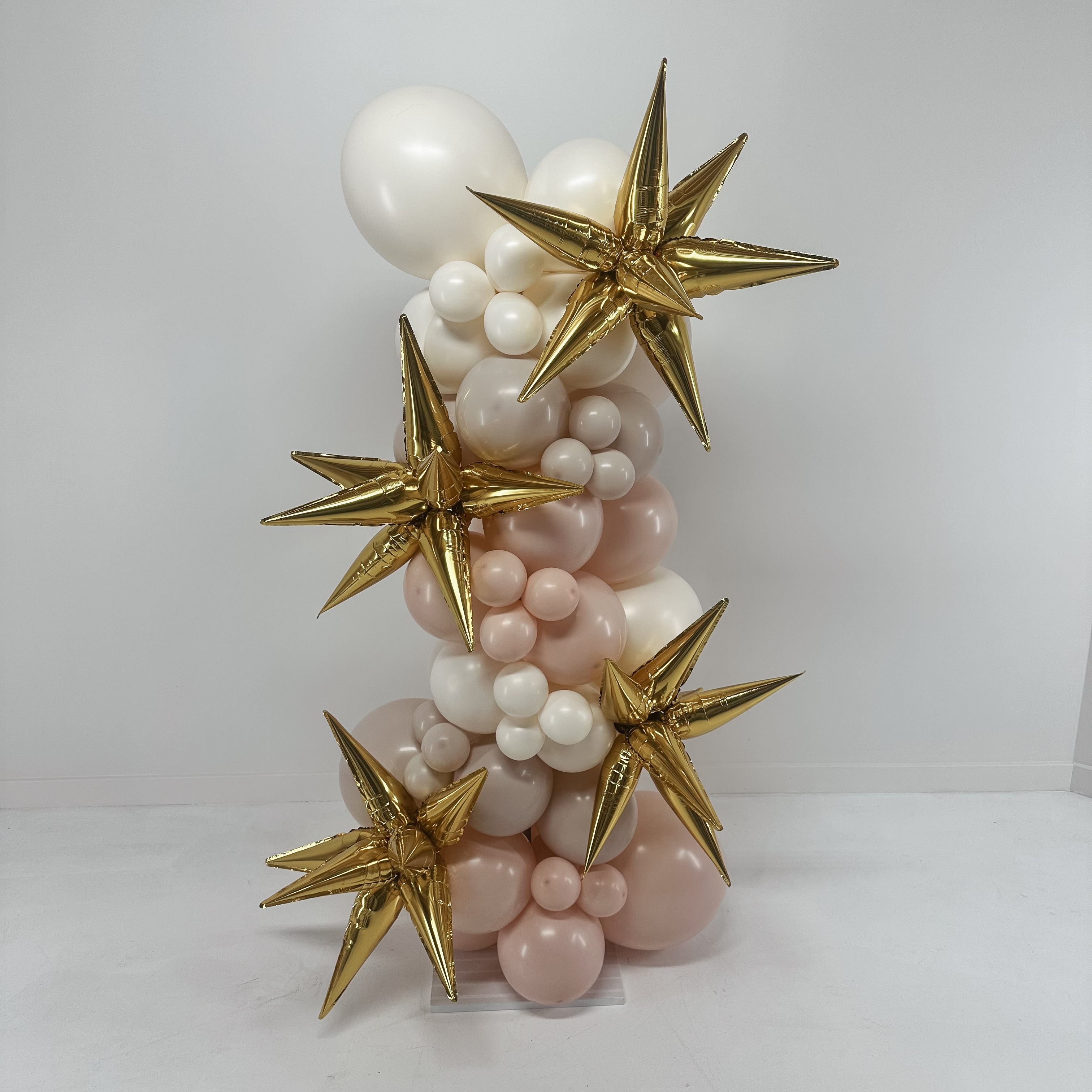 Balloon sculpture with gold stars and white and pink balloons on a white background