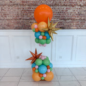 Colorful balloon sculpture with stars against a brick wall.