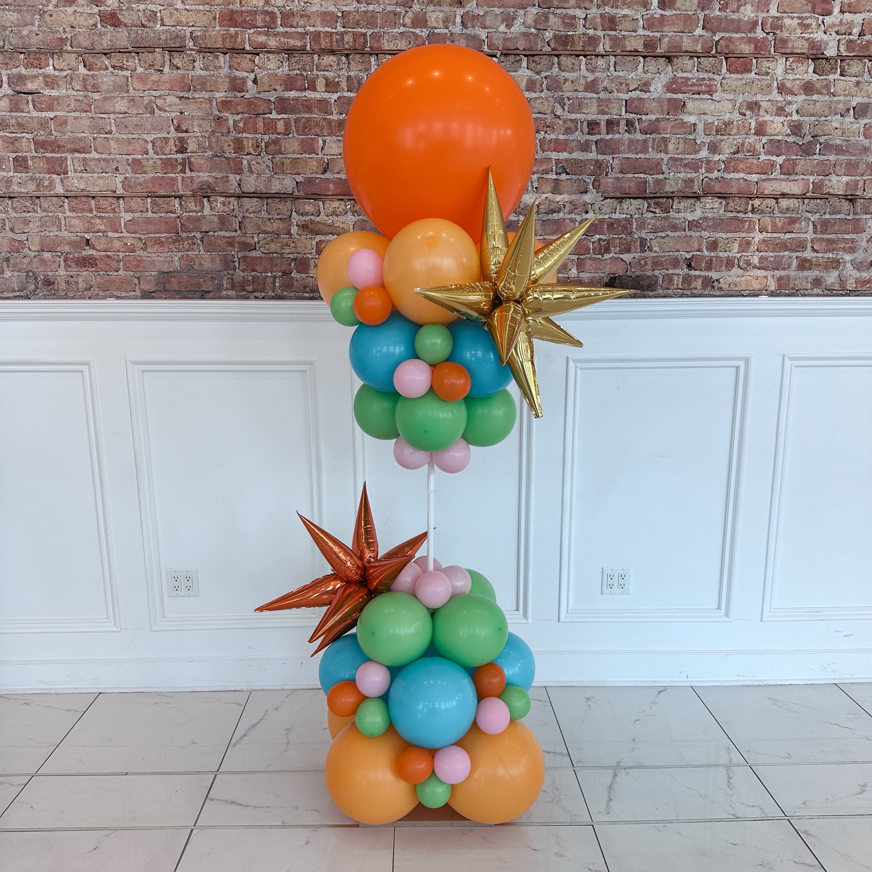 Colorful balloon sculpture with stars against a brick wall.