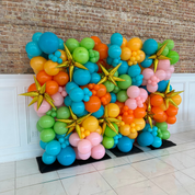 Colorful balloon arrangement with gold stars against a brick wall.